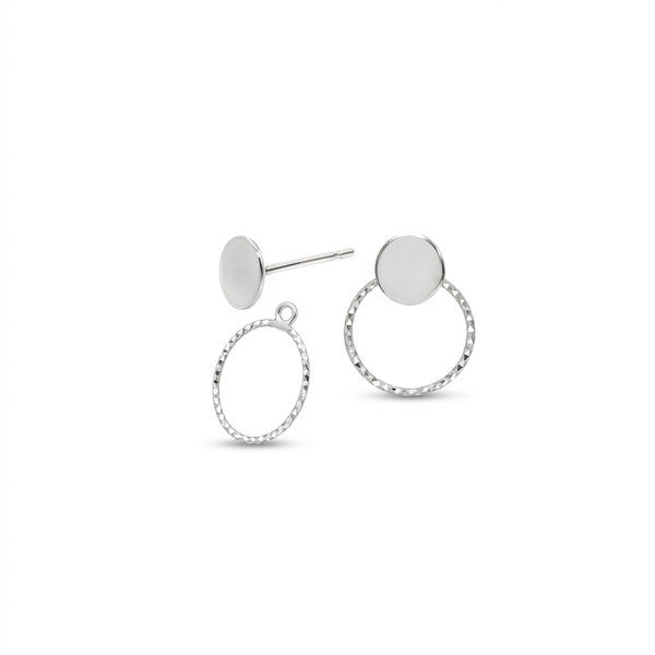 A pair of silver stud earrings featuring a flat circular disc on one earring and a textured oval frame with a matching disc on the other, shown on a plain white background.